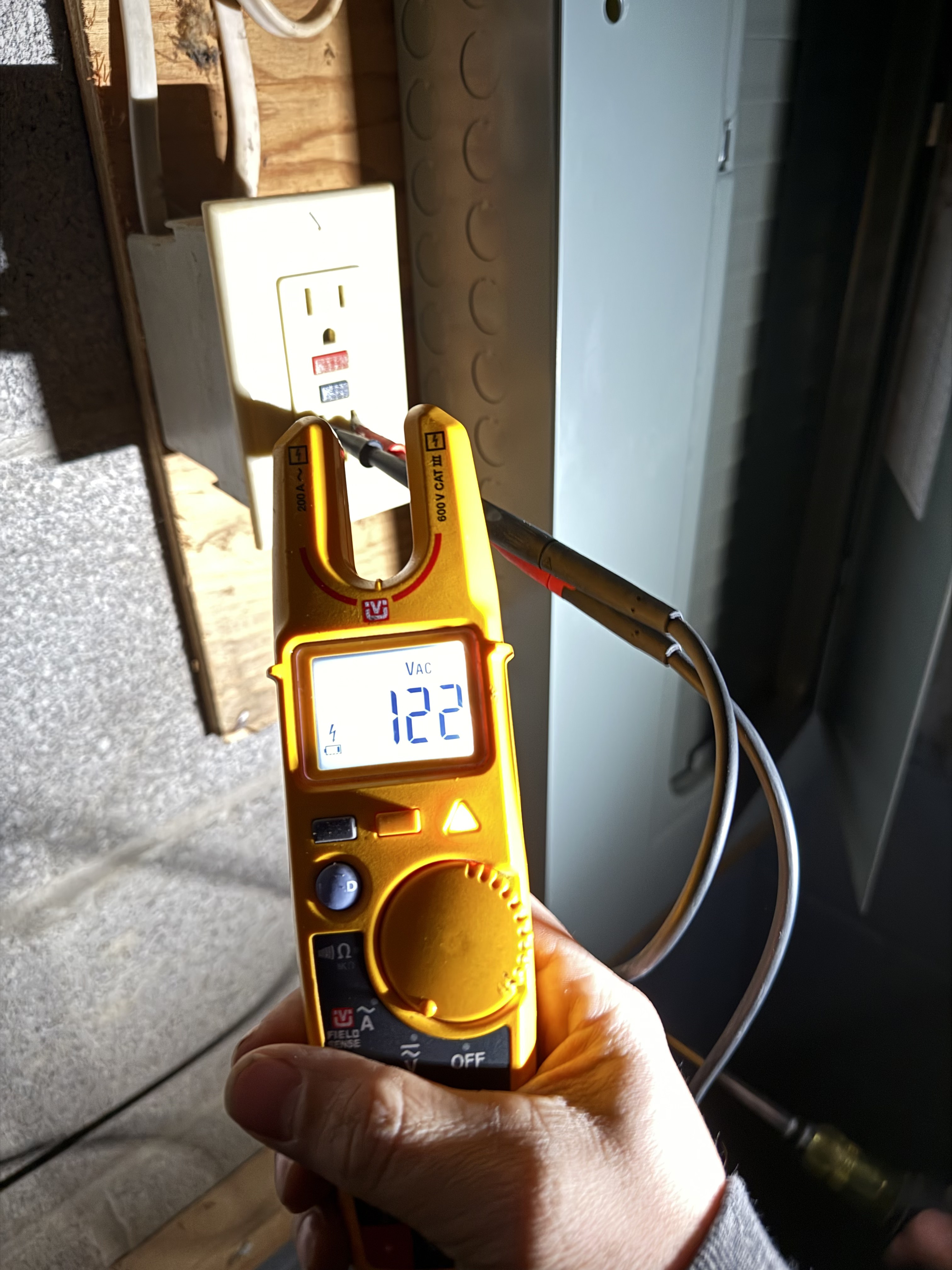 Electrician troubleshooting outlet voltage with clamp meter during emergency electrical service call in Rochester NY
