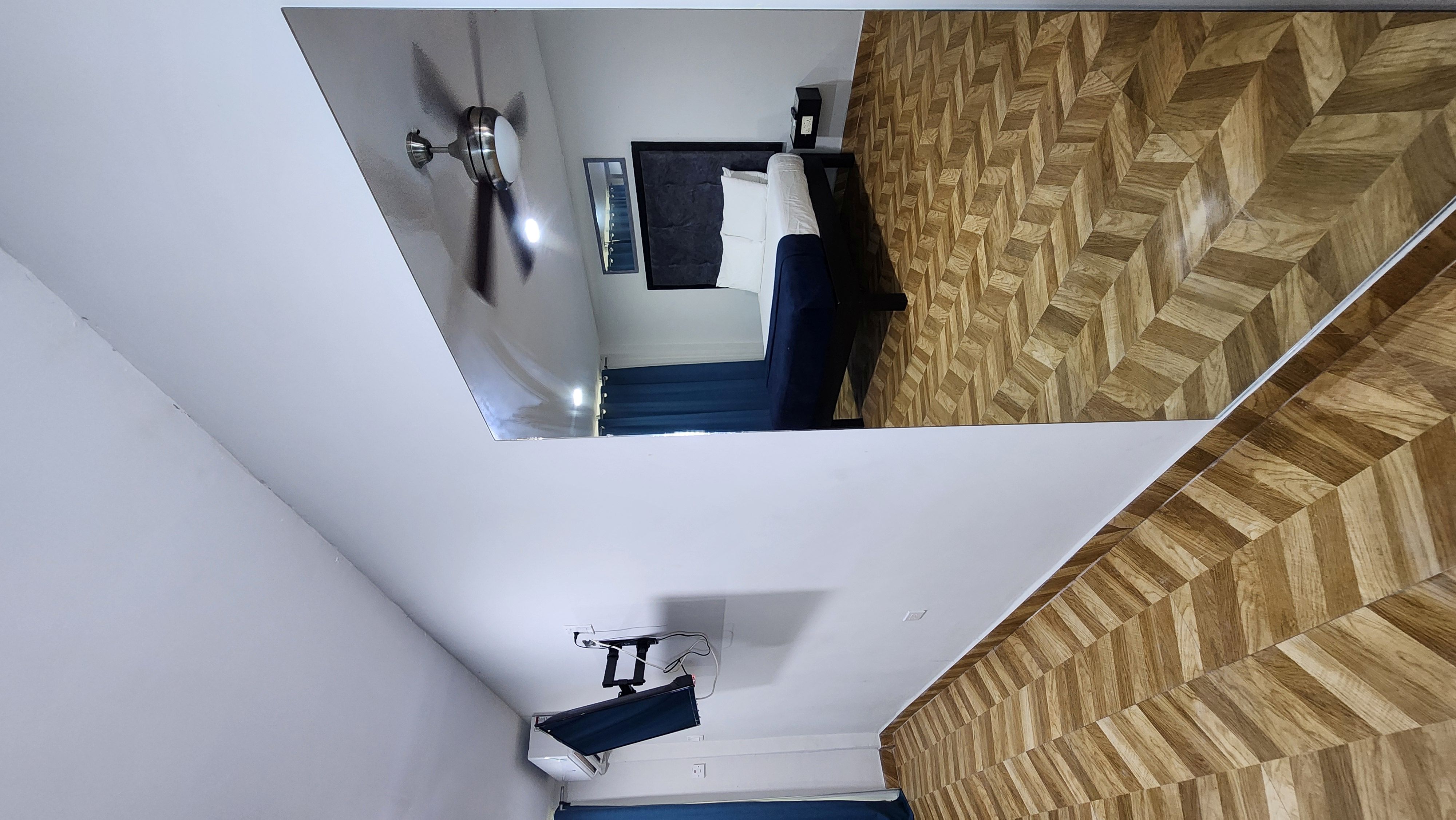 MG6 room reflected in mirror — ceiling fan, navy headboard, herringbone floors