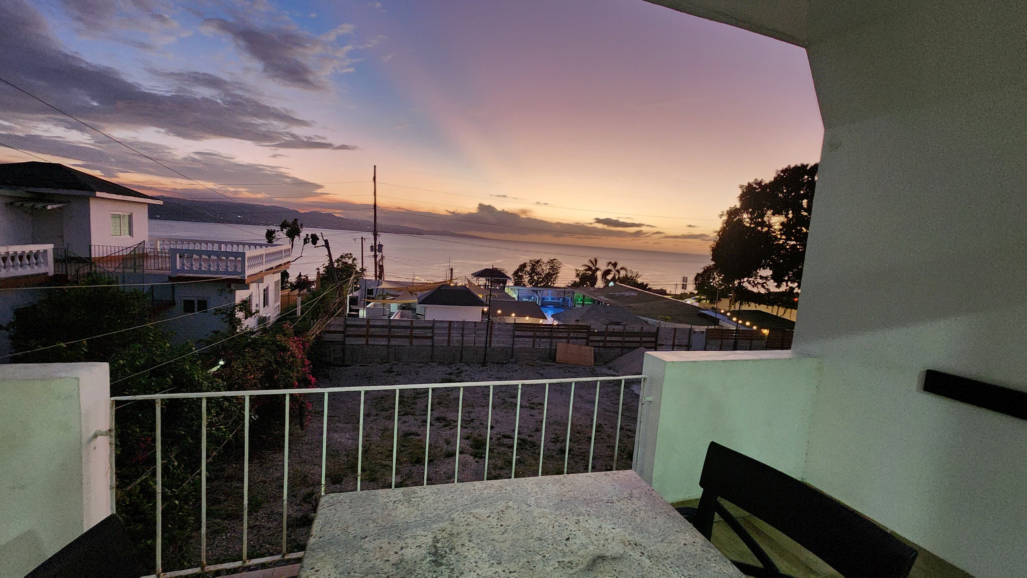 MG17 private balcony at sunset — panoramic ocean view, pink and orange sky, pool and bar below