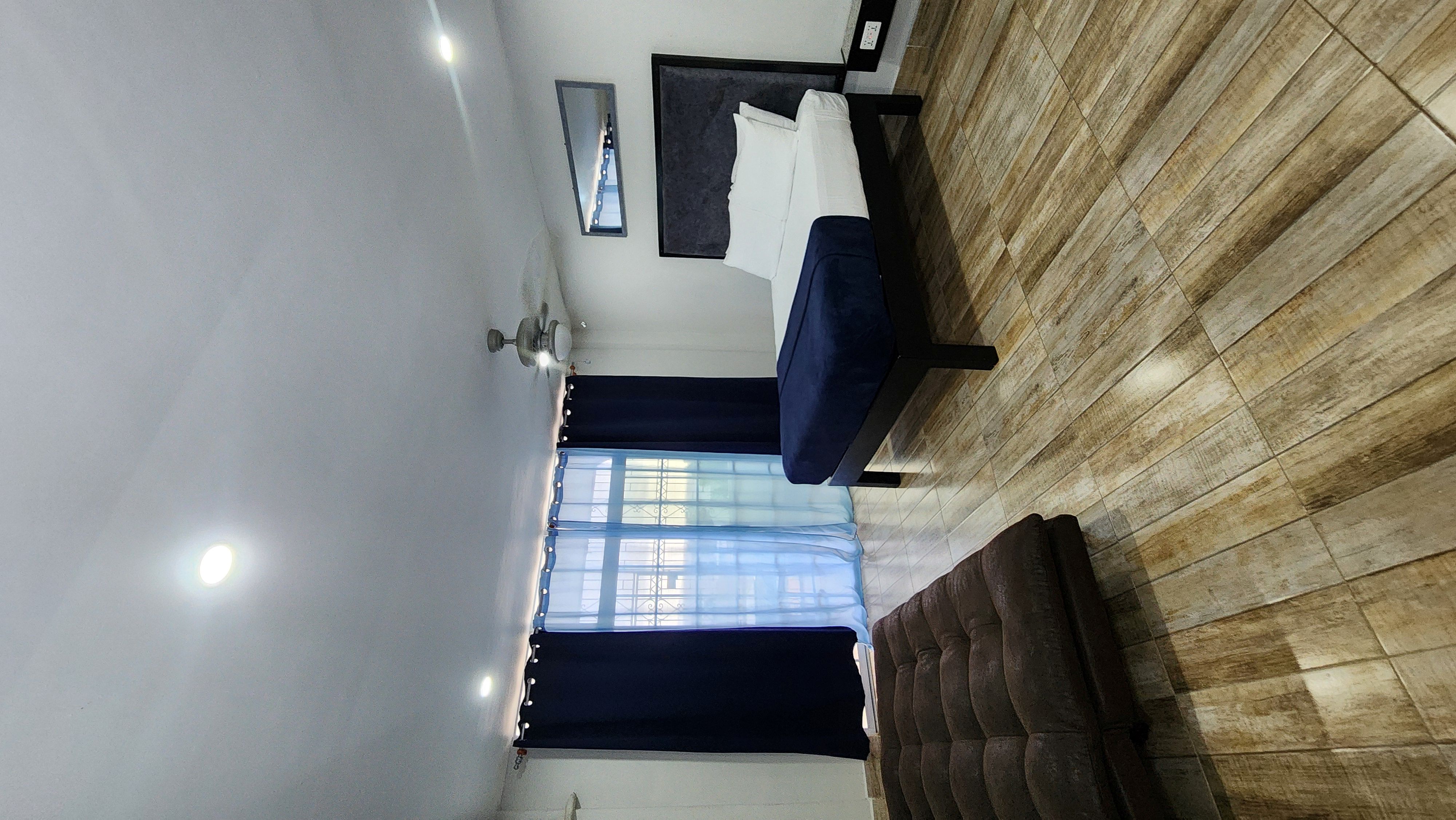 MG7 queen bed and futon sofa — navy blue curtains, ceiling fan, natural light