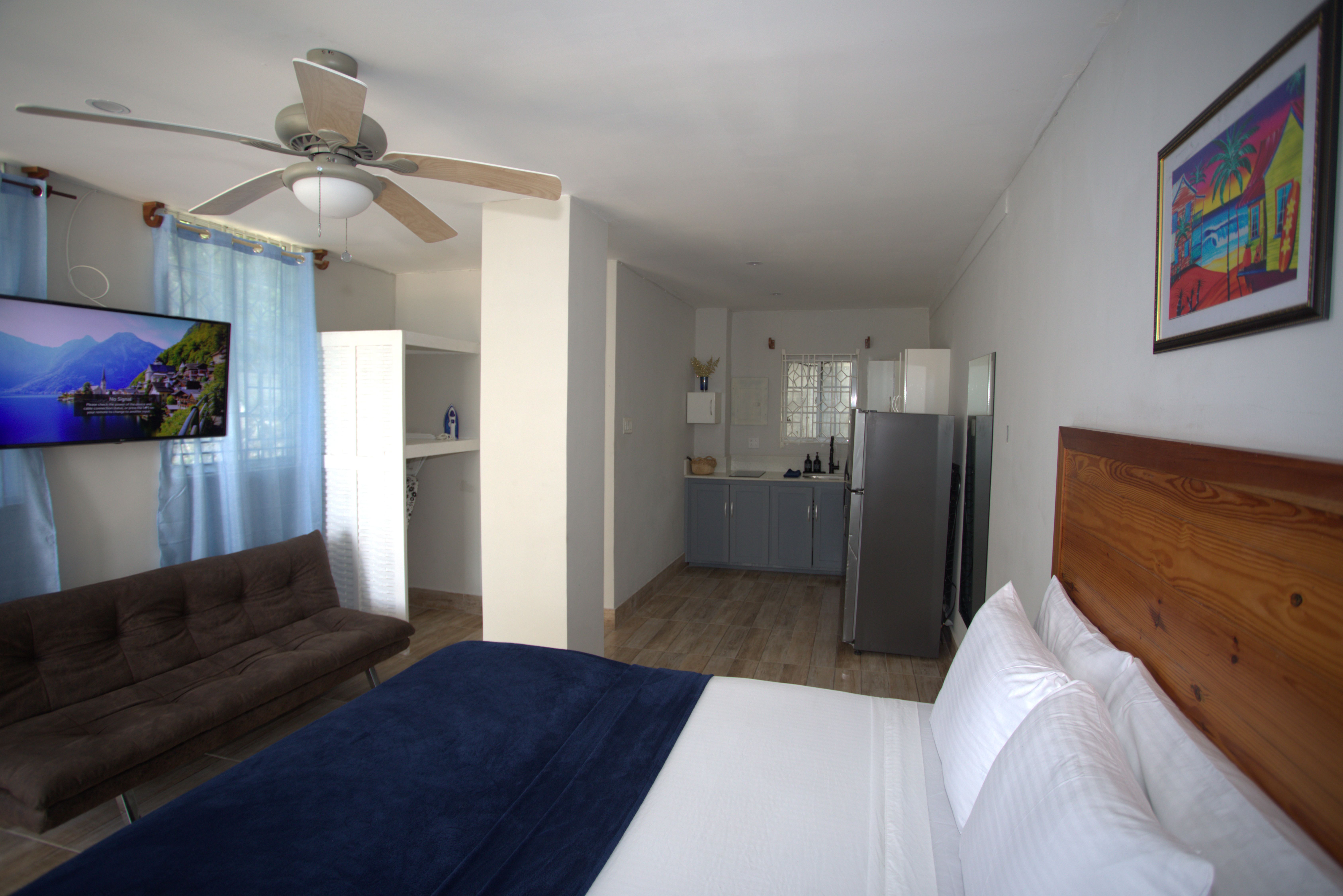 Montego Gardens MG1 studio — queen bed, futon sofa, full kitchen, ceiling fan, Smart TV, and Caribbean artwork