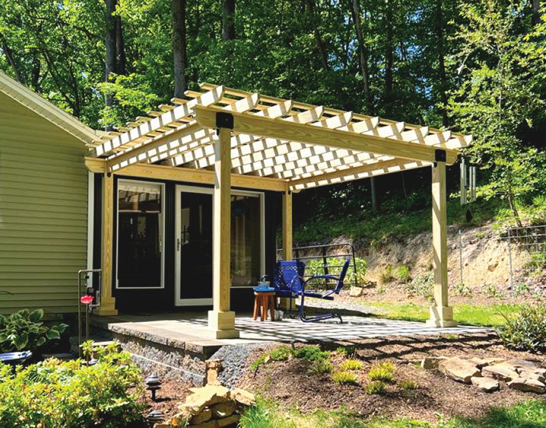 Natural pressure-treated wood Hollander pergola beside a house, with a blue chair on a stone patio