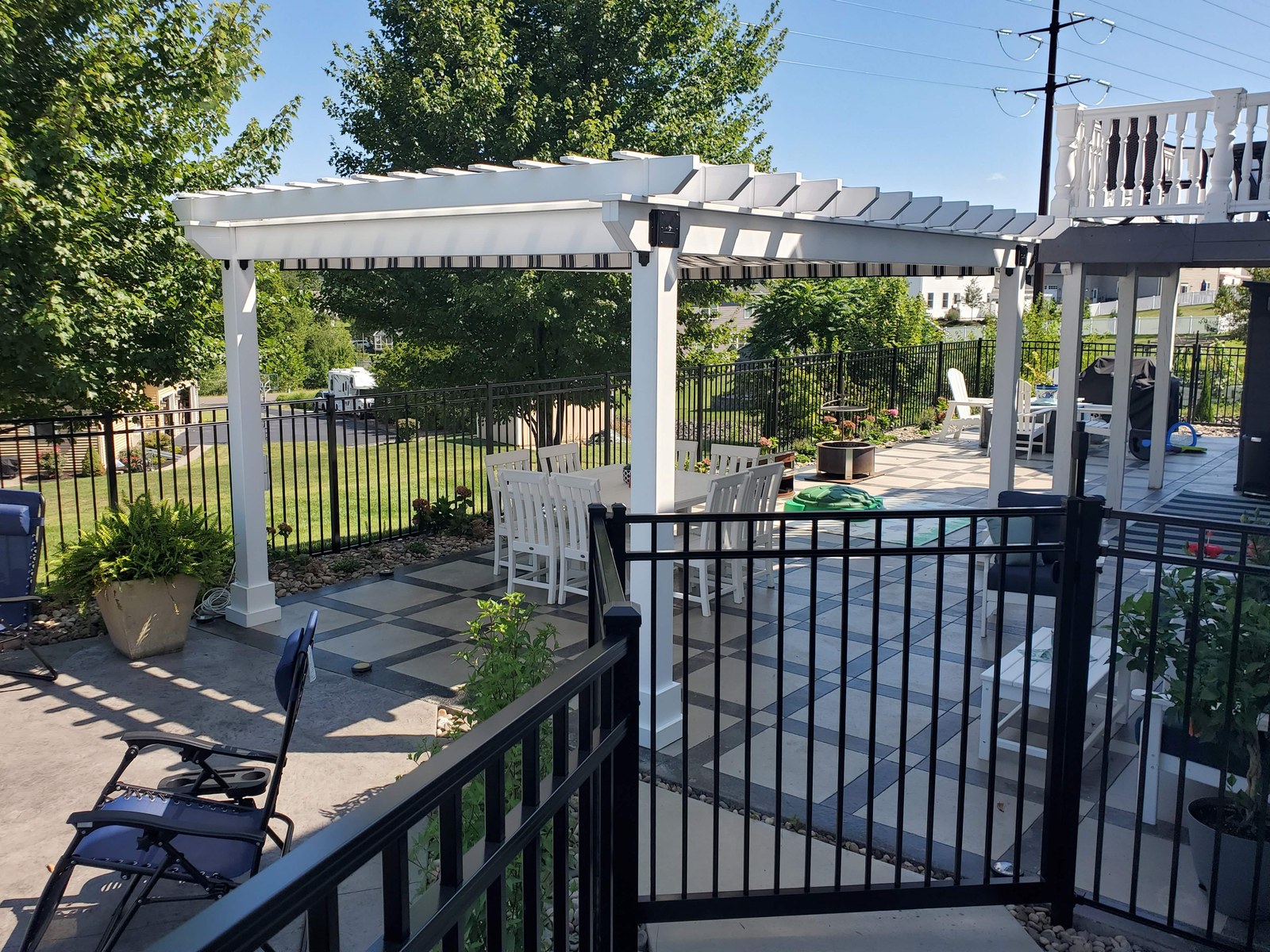 White vinyl Hollander pergola with an awning over a patterned paver patio, with a white dining set underneath