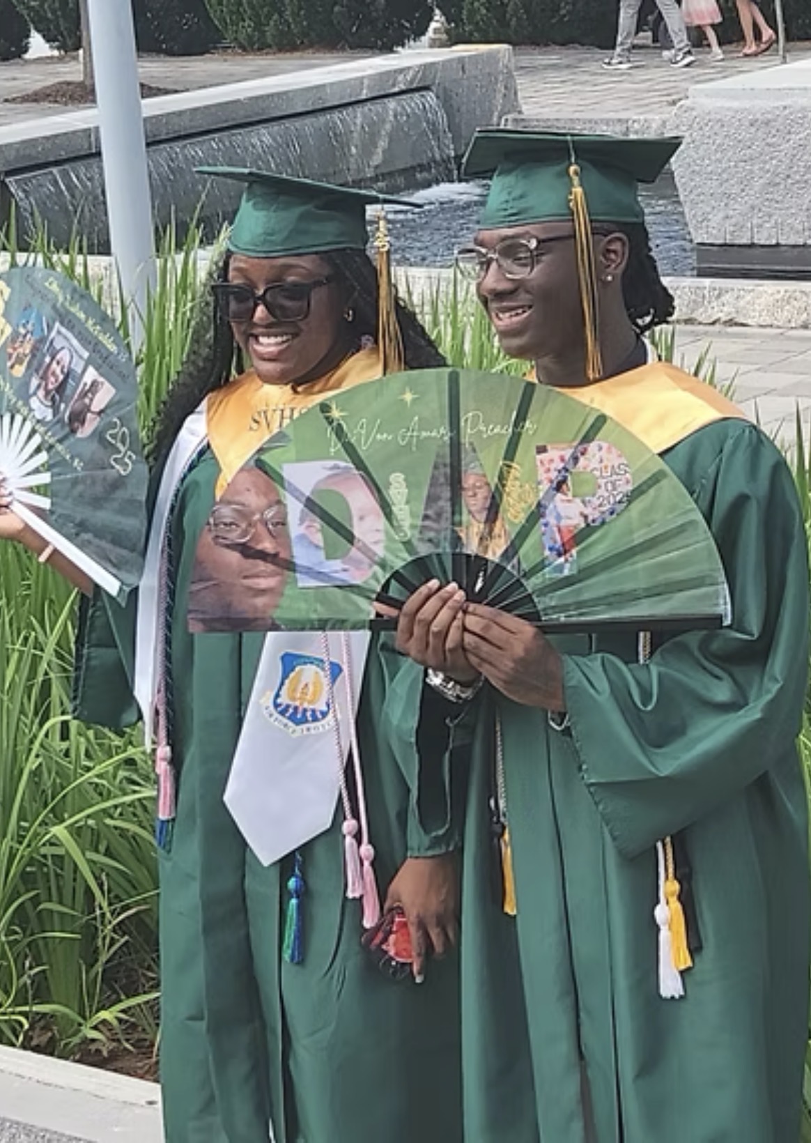 Two graduates celebrating together with fans and tassels
