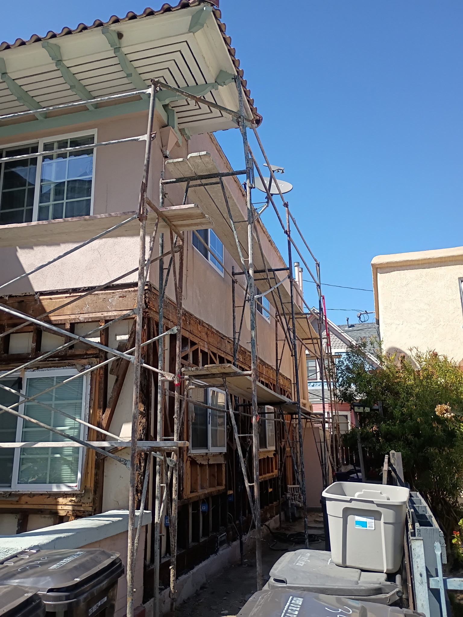 Two-story building with scaffolding — stucco removed exposing framing and lath, major repair by PMR Projects