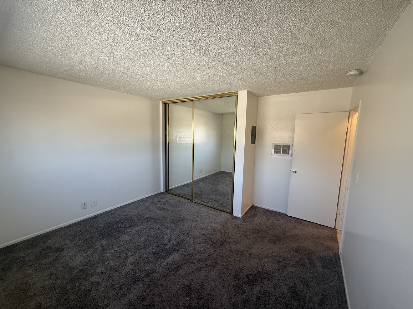 Bedroom before flooring installation — worn dark carpet with mirrored closet doors, Long Beach rental unit
