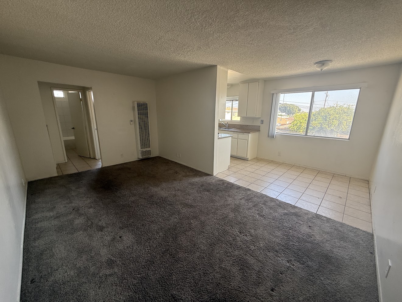 Living room before flooring installation — worn dark carpet with tile kitchen area, Long Beach rental unit