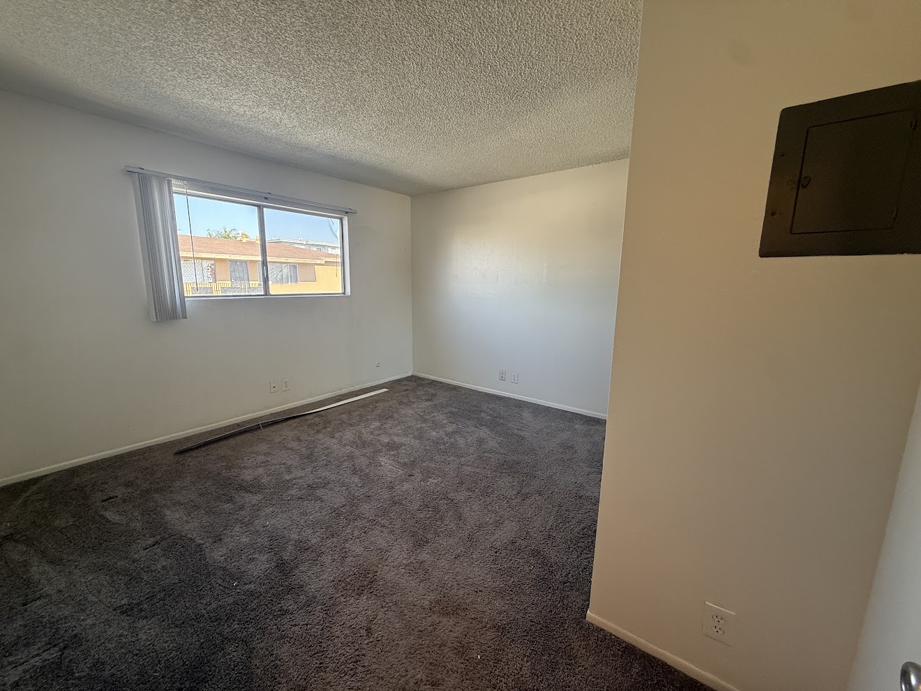 Bedroom before flooring installation — worn dark carpet with access panel, Long Beach rental unit